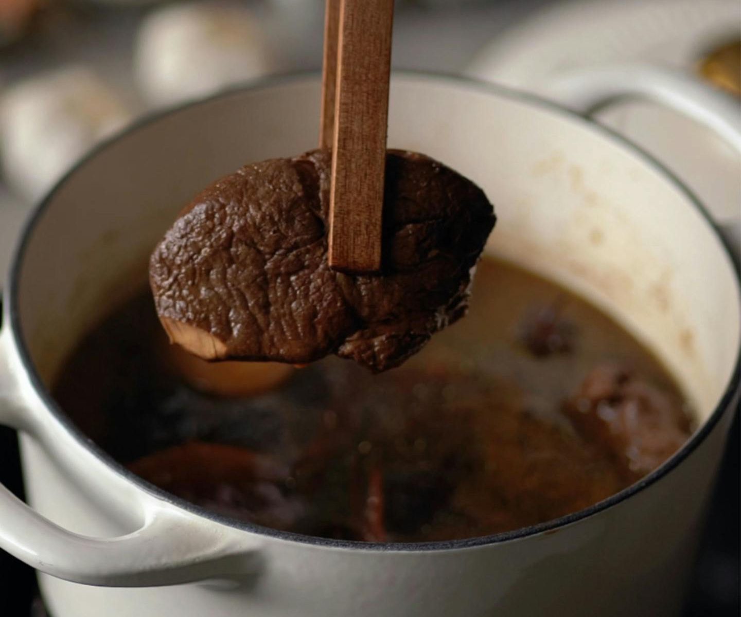 Close-up of hand cooking rich meat stew in pot, depicting home-cooked meal preparation.