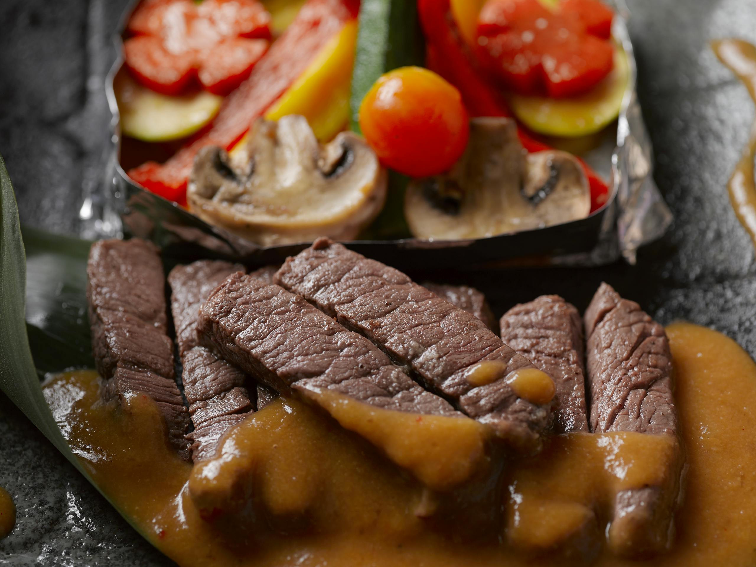 Succulent beef slices with savory sauce, paired with fresh grilled vegetables. Perfect gourmet meal.
